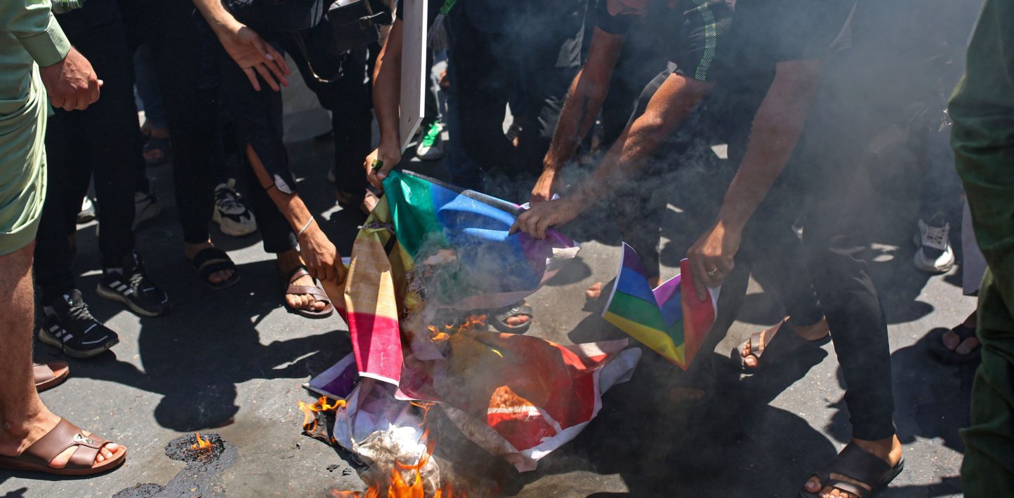 Supporters of Iraq's Sadrist movement burn posters depicting the LGBTQ+ flag during a protest in Basra on June 30, 2023, denouncing the burning of Islam's holy book in Sweden. The protest came a day after an Iraqi citizen living in Sweden, Salwan Momika, 37, stomped on the Islamic holy book and set several pages alight in front of the capital's largest mosque. Swedish police had granted him a permit in line with free-speech protections, but authorities later said they had opened an investigation over "agitation". (Photo by Hussein FALEH / AFP) (Photo by HUSSEIN FALEH/AFP via Getty Images)