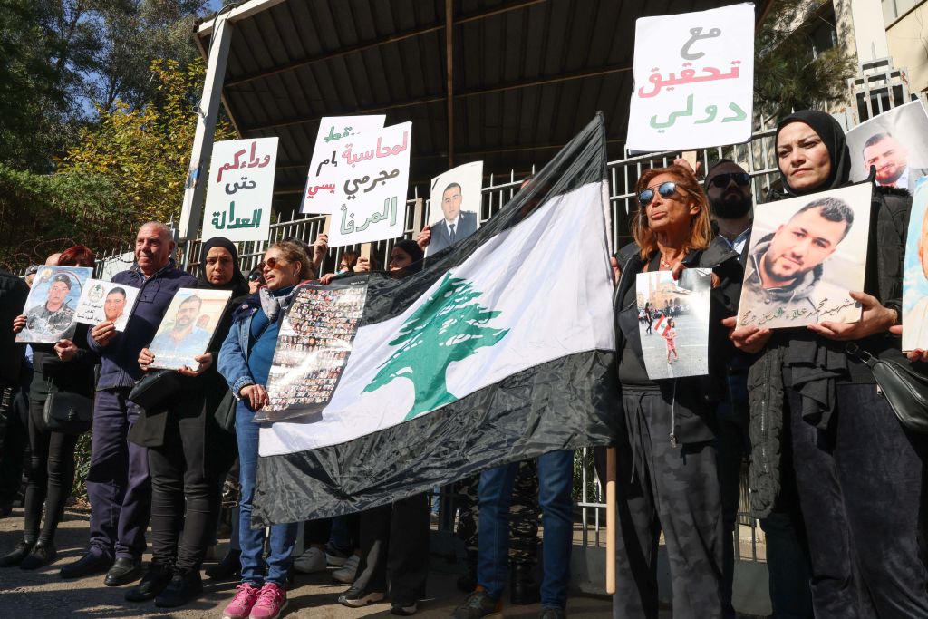 Relatives of victims of the 2020 Beirut port explosion, hold posters bearing images of people killed in the blast, as well as a national flag with black stripes instead of the official red color of the flag, during a rally outside the palace of justice to support the judge investigating the disaster, on January 26, 2023.
