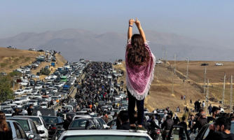 Photo shows an unveiled woman with her back to the camera showing her long hair and pink scarf over her shoulder standing on top of a vehicle as thousands make their way toward Aichi cemetery in Saqez, Mahsa Amini's hometown in the western Iranian province of Kurdistan, to mark 40 days since her death.