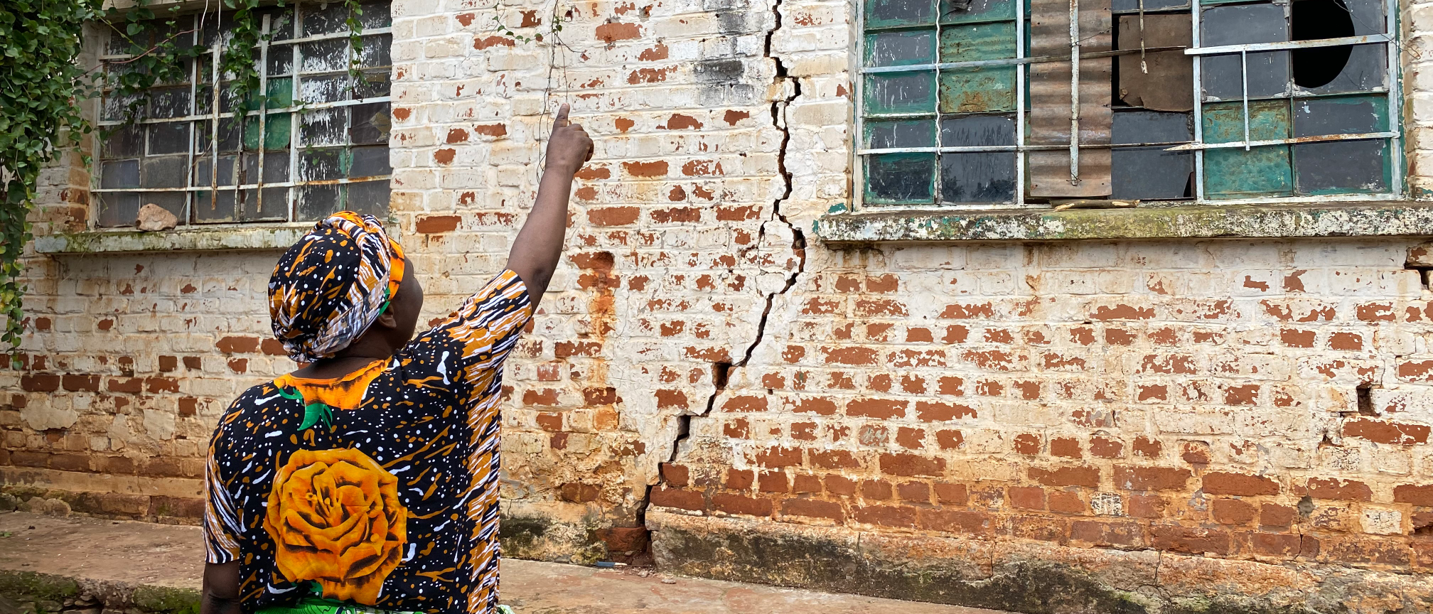 A woman points upwards at a large crack in the wall of her house