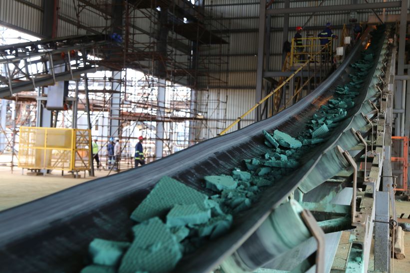 A long conveyor belt carrying large blue green chunks of raw cobalt.