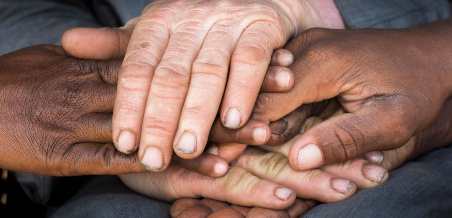 Several people's hands, of different skin tones, resting on top of each other.