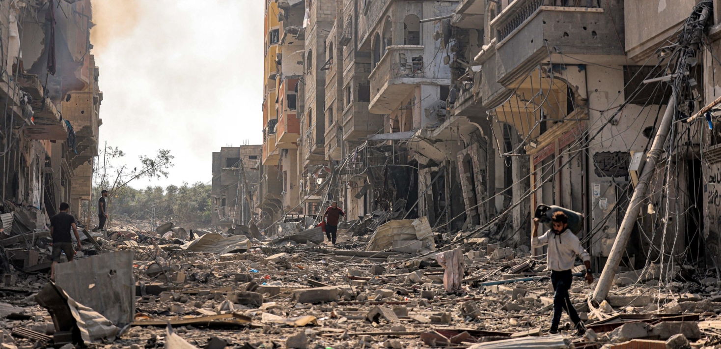 Complete rubble and destroyed buildings following a bombing. A man is seen walking in between the rubble.