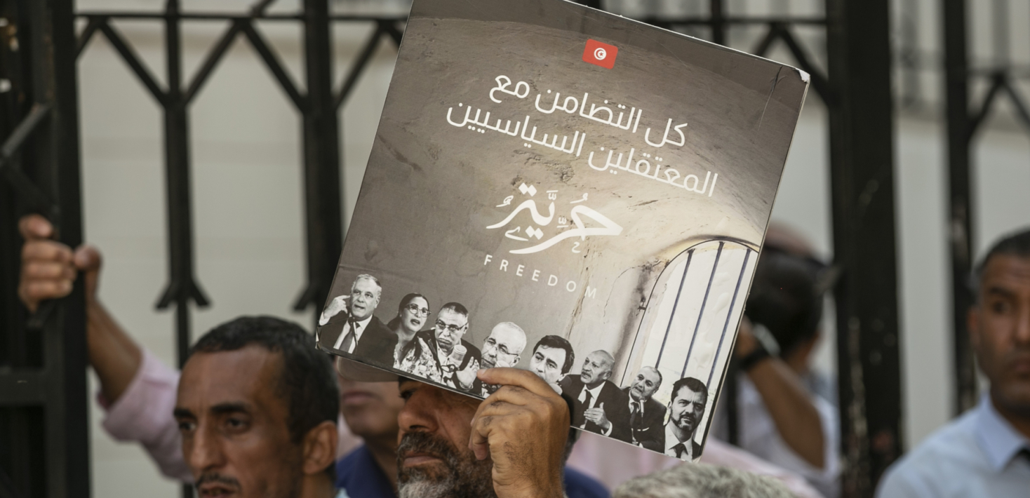 Tunisian activists are seen during a protest calling for the reslease of political detainees and one in center holding a placard with an image in black and white with the word "freedom" in Arabic in the middle and the portraits of the political opponents being held.