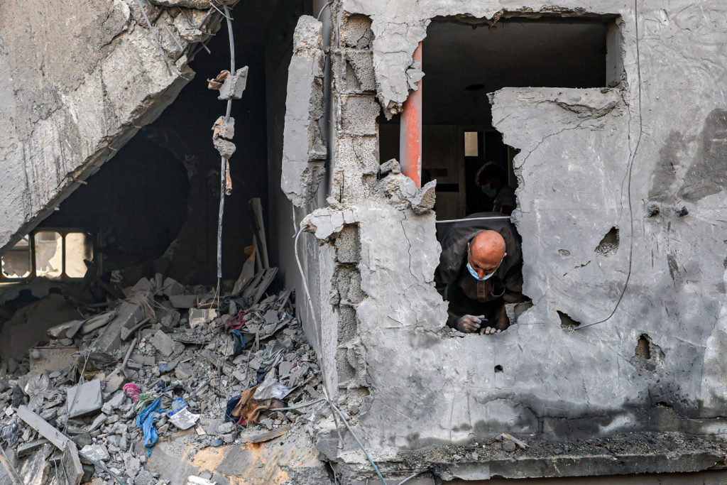 Un hombre mira a través de un hueco en un edificio, mientras la gente busca sobrevivientes y los cadáveres de las víctimas entre los edificios destruidos por el bombardeo israelí sobre Jan Yunis, en el sur de la Franja de Gaza el 25 de octubre de 2023.