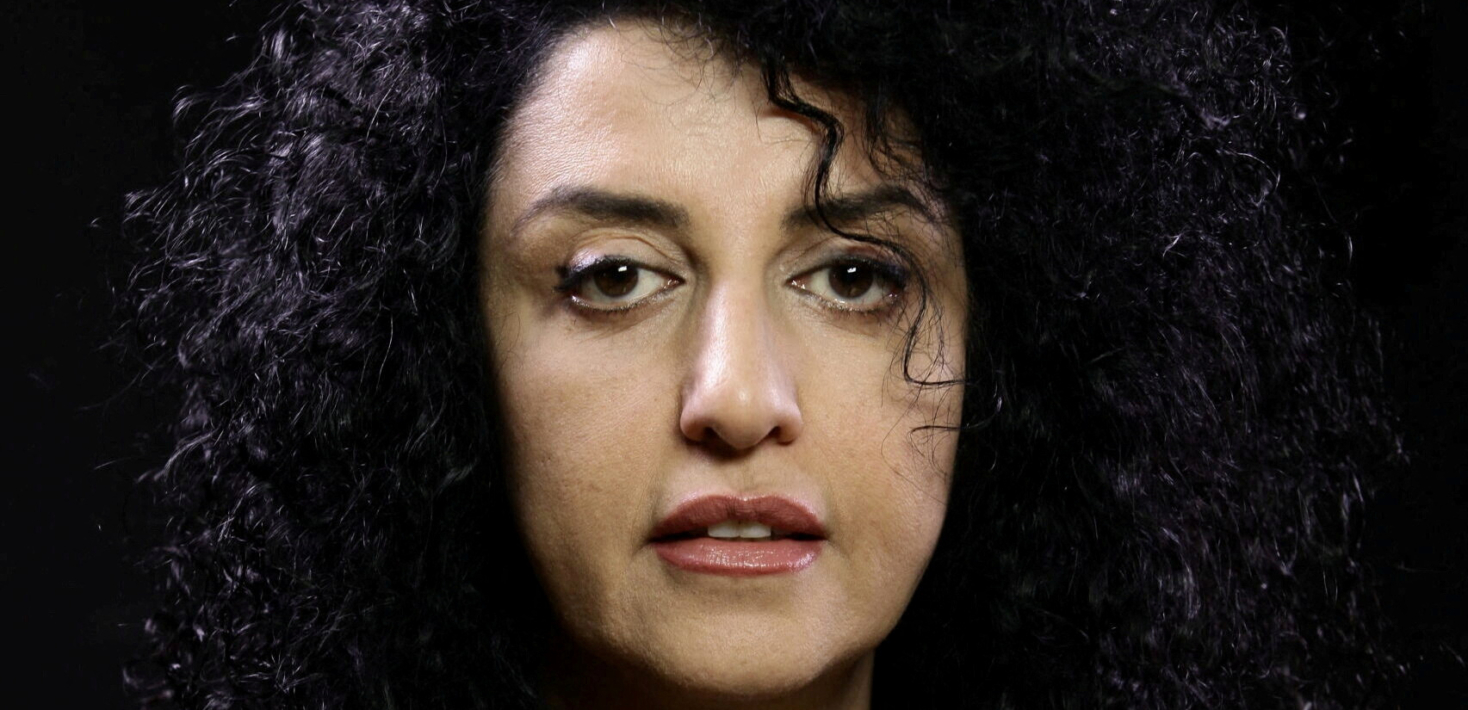 Portrait photo of Nobel Peace Prize Winner Narges Mohammadi without wearing the traditional Hijab, showing her black curly hair, black eyes and wearing a velvet burgundy shirt