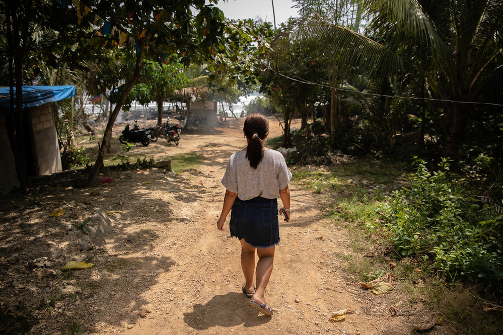 Marinel is walking away from the camera down a dirt path. She is surrounded by lush gree trees and foliage.