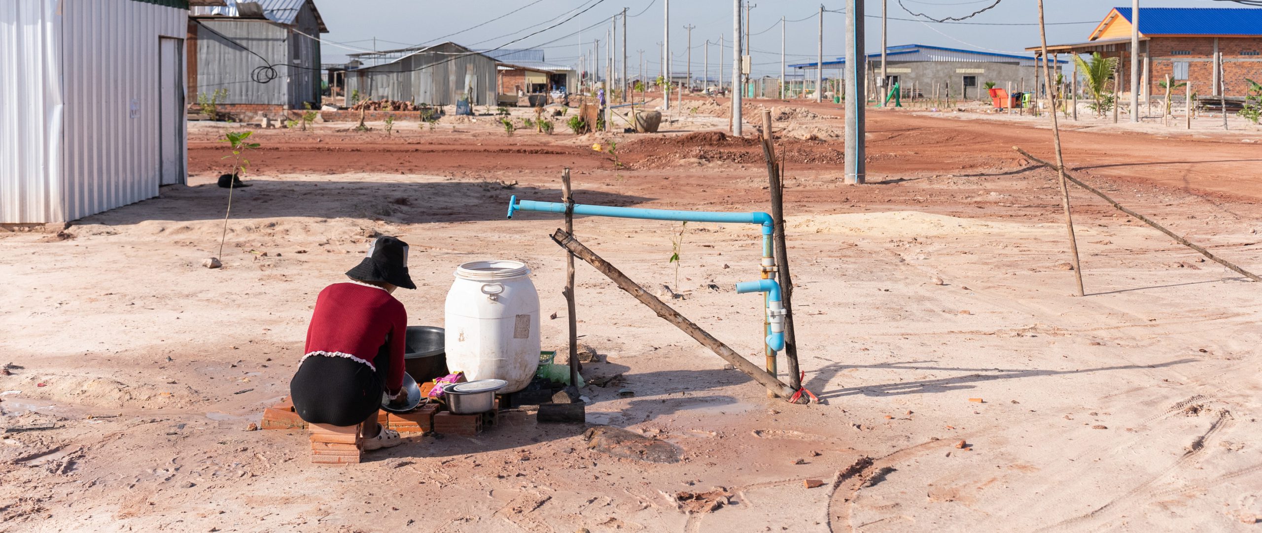 Foto tomada en julio de 2023 en la que una residente lava ropa usando una de las bombas de agua instaladas por las autoridades para las viviendas del sitio de reasentamiento de Run Ta Ek.  Según la investigación de Amnistía, el lugar de reasentamiento está creciendo a medida que llegan nuevos residentes, pero faltan servicios esenciales.