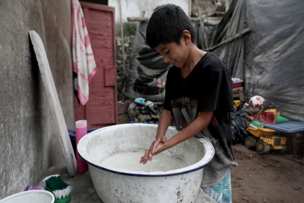 a young boy washes his hands in a large basin. There is no running water. 