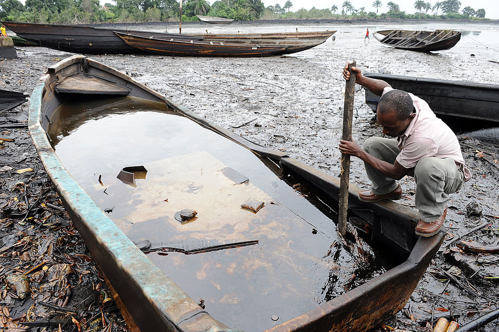 A man expects his boat in a creek damaged by severe oil pollution in the Niger Delta