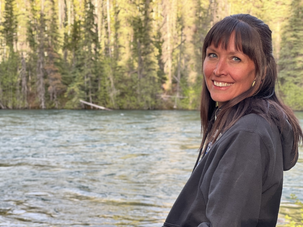 Molly Wickham, also known as Sleydo’, a Wet’suwet’en land defender, stands in front of a river, smiling.
