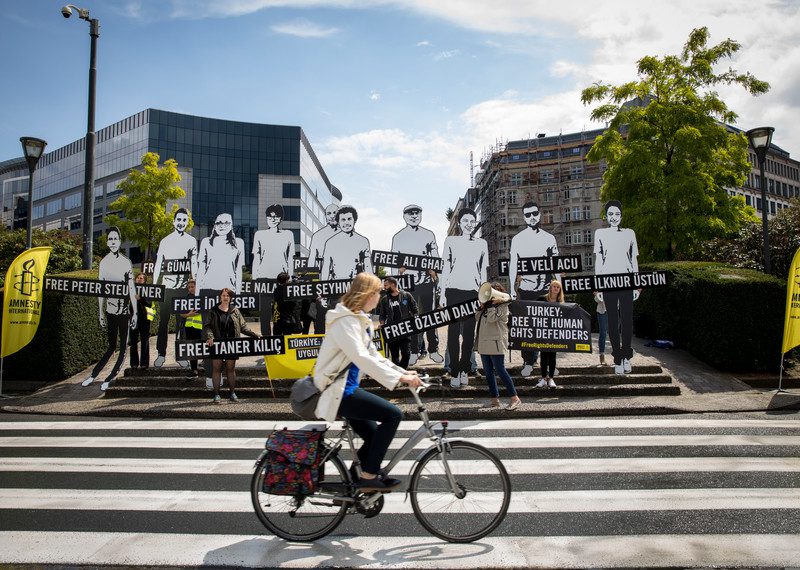 Activists stand on steps, holding signs that read Free Taner Kilic amongst others.