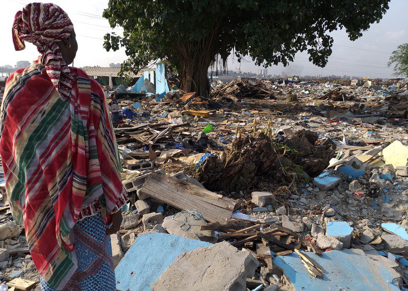 A person looks out over the ruins of destroyed buildings stretching into the distance.