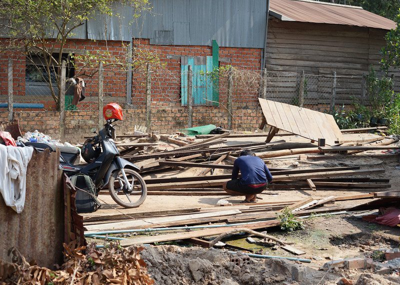 A house has been smashed to pieces while a solitary man crouches in front of it.