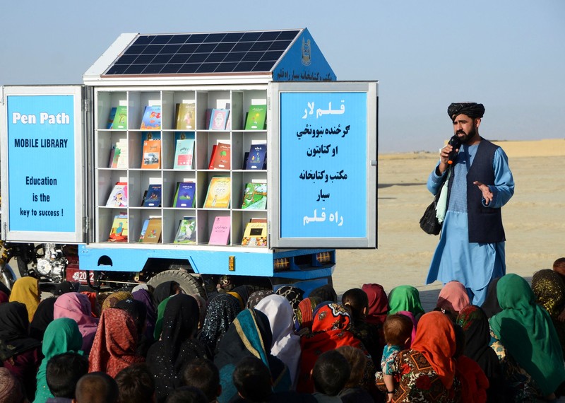 Children sit on front of a small blue truck that doubles up as a mobile library.
