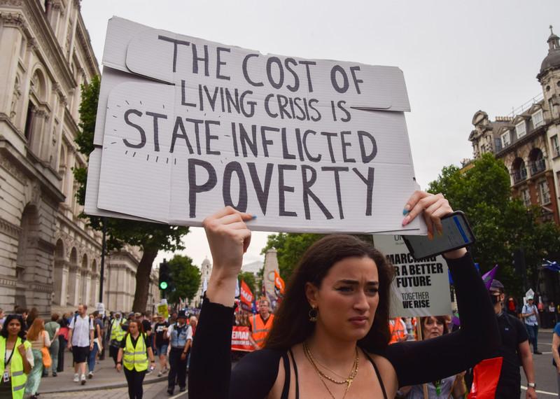 Person at a protest holding up a sign which reads 'the cost of living crisis is state inflicted poverty'