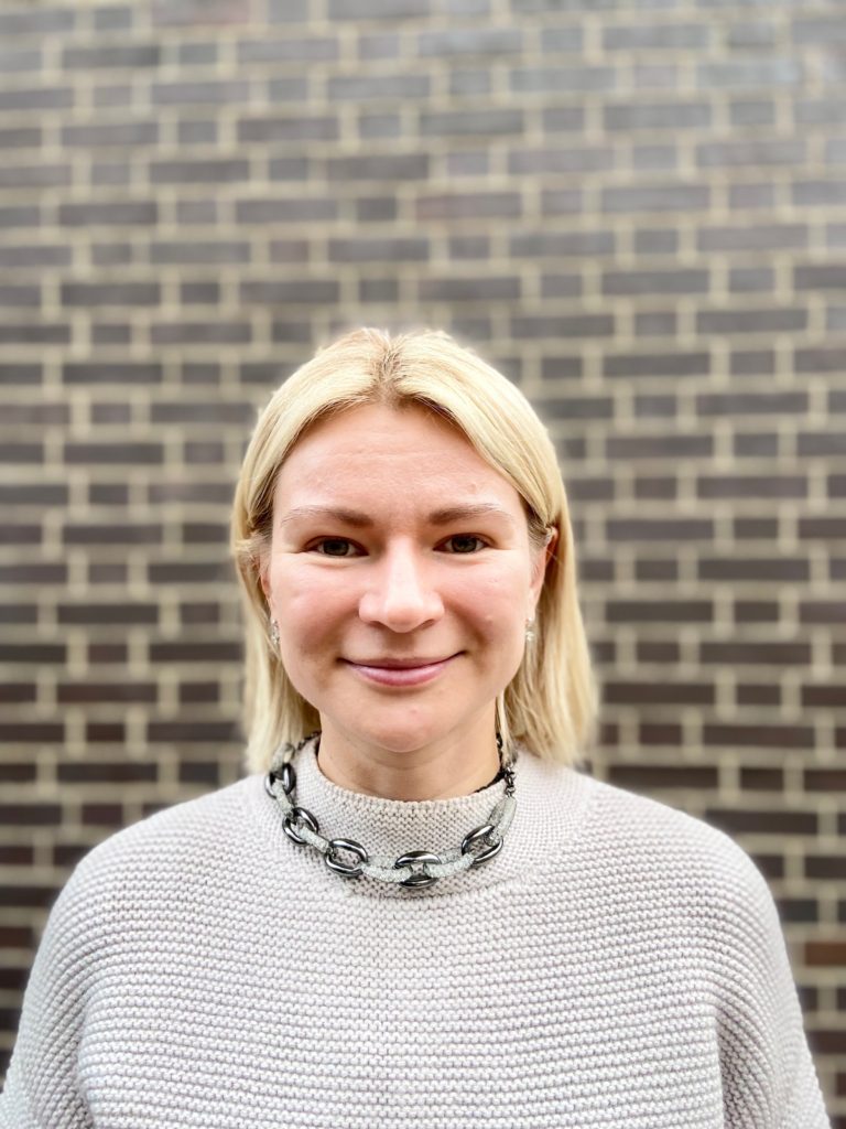 La investigadora de Amnistía, Anna Wright, sonríe delante de una pared de ladrillo. 