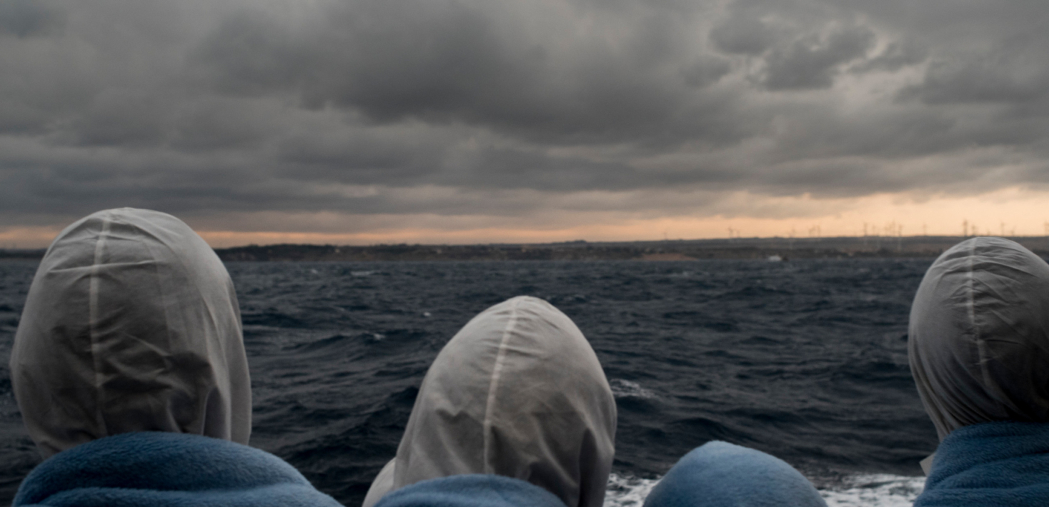 Migrants on boat looking at land ahead