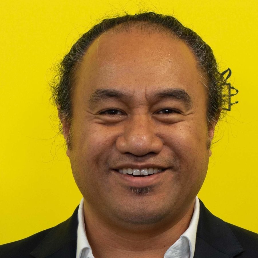 Peter Fa'afui in front of a yellow background with the amnesty logo. He is wearing a white collared shirt and jacket.