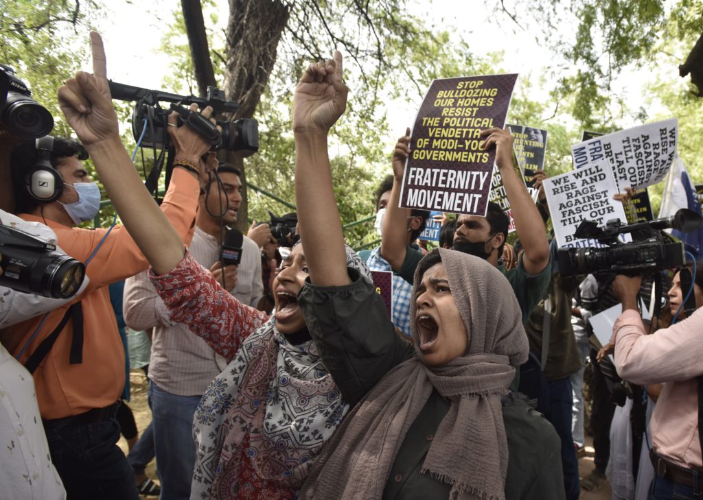 A group of activists protest against the demolition. They have their fists raise and are chanting. Some are carrying placards.