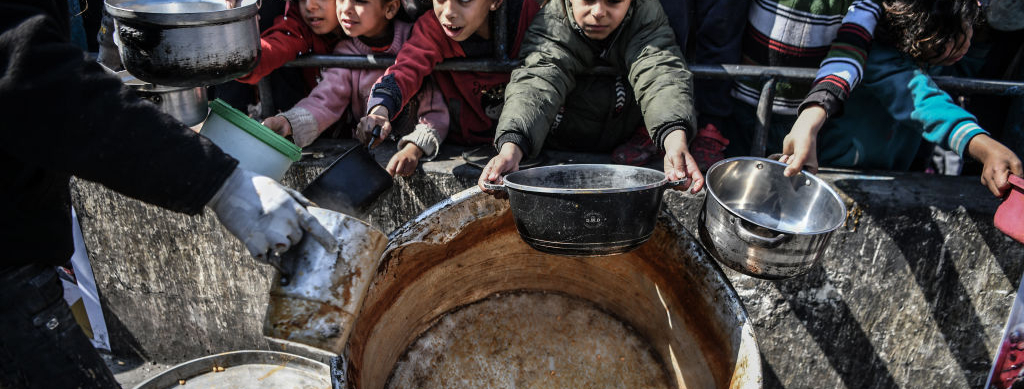Palestinians hold out their empty containers to be filled with food, distributed by charity organizations, behind bars since they are unable to obtain basic food supplies due to the embargo imposed by Israeli forces in Rafah, Gaza on February 25, 2024.