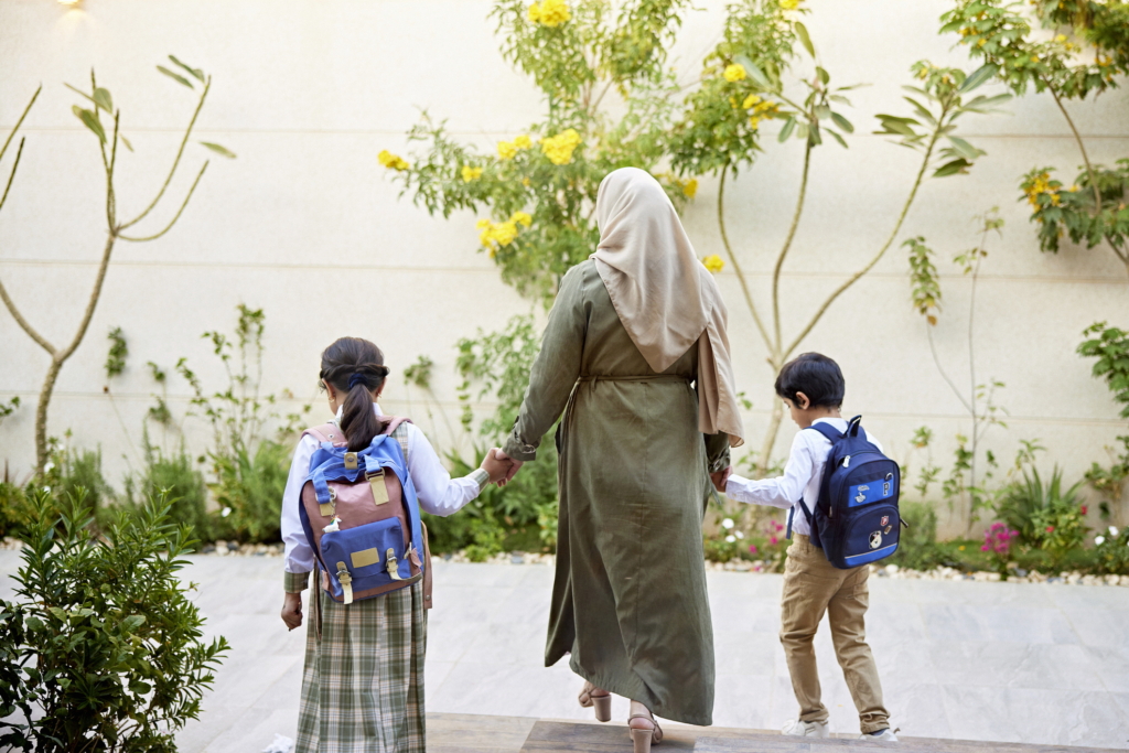 امرأة ترتدي حجابًا مع طفلين. ويحمل كل من الطفلين حقيبة ظهر زرقاء اللون.