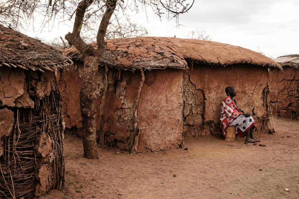 A Maasai woman sits in front of a thatched home 
