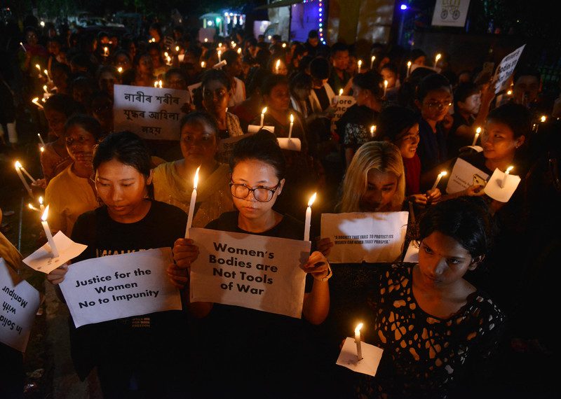 A crowd of people hold candles and placards denouncing violence against women. 