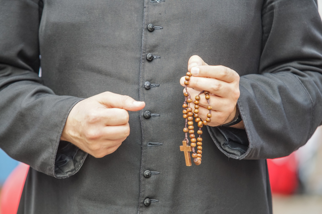 a close up shot of someone in black priest robes holding a rosary