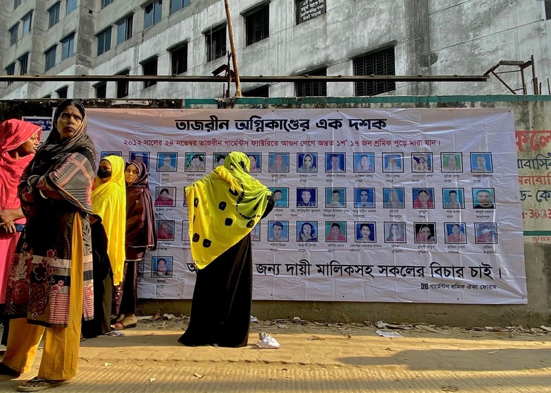 Women stand in front of a banner showing those who lost their lives.