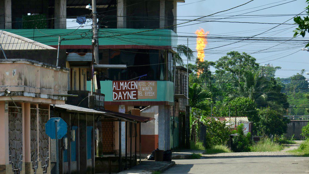 A street with a flame over the trees in the distance.