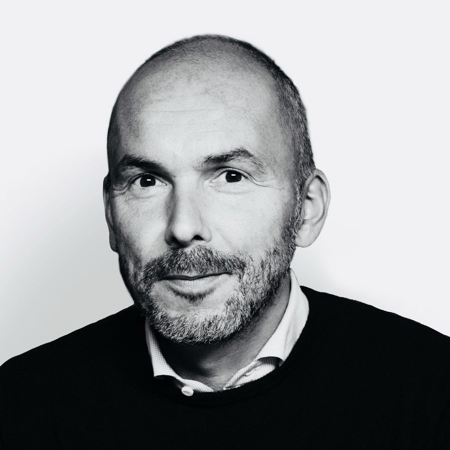 Black and white portrait of Christopher wearing a dark jumper against a white background.
