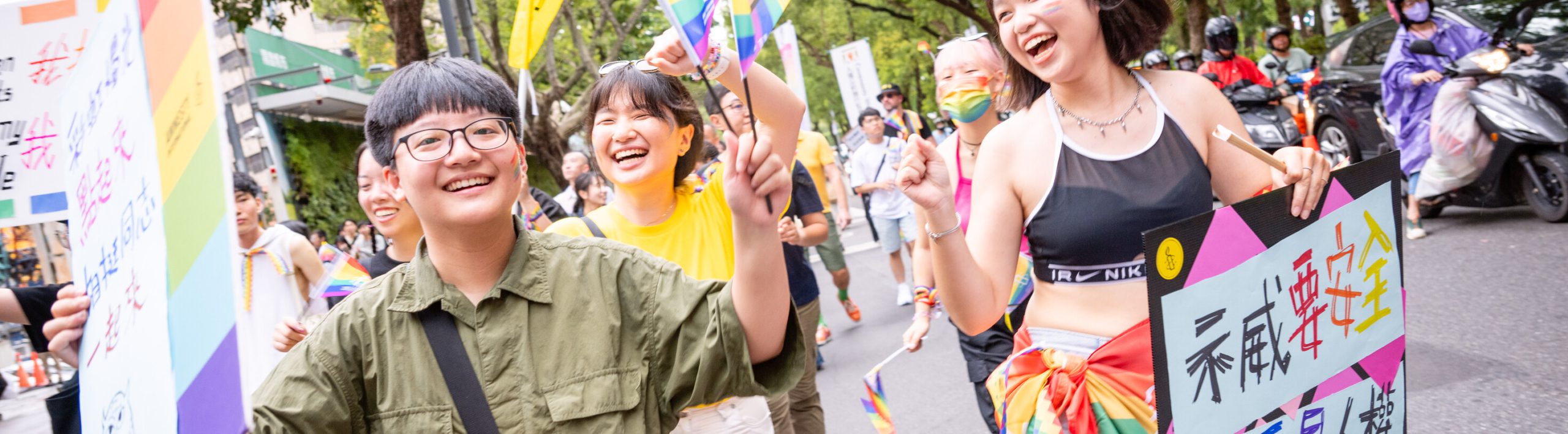 A group of people walk down the street holding colourful flags high.