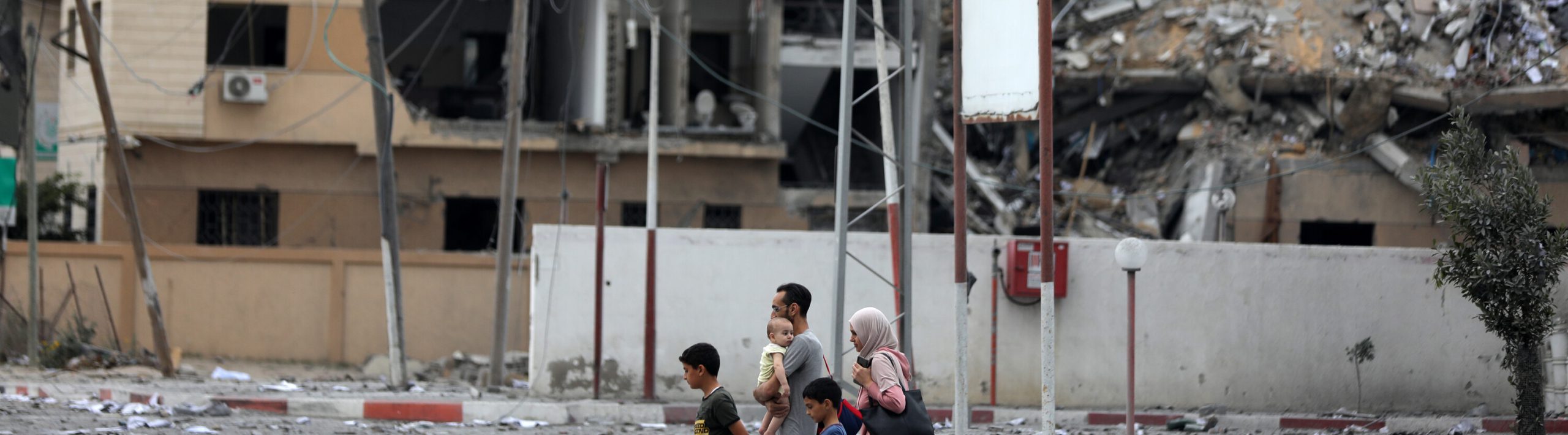a family walk together in front of a building that has been destroyed.