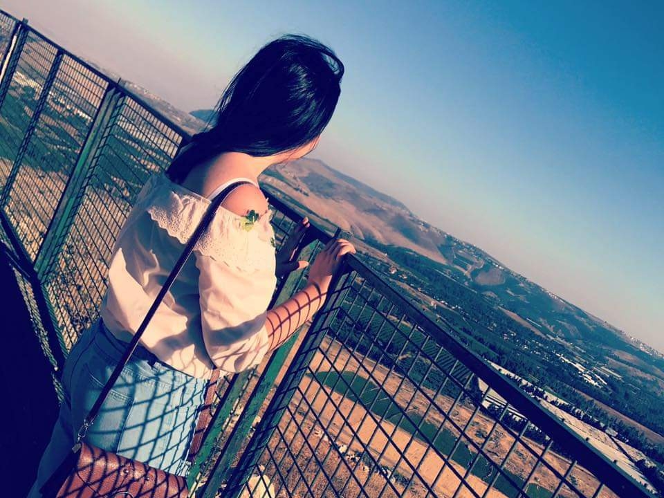 A woman stands near a fence overlooking a rural landscape