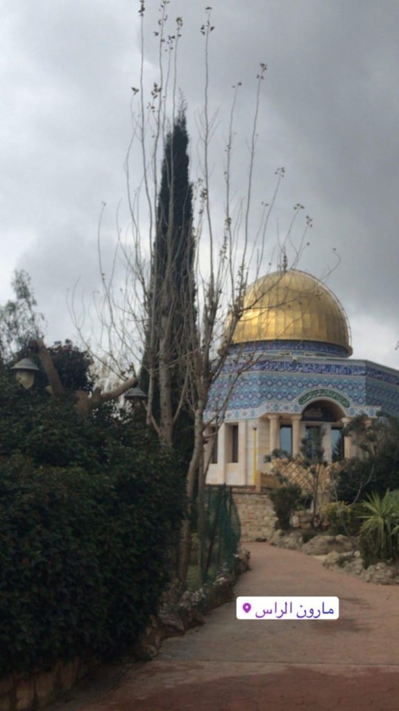 A blue mosque with a golden dome is pictured in a garden