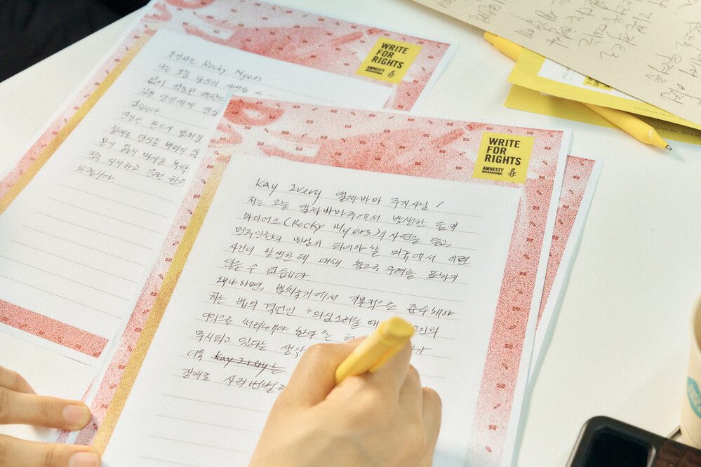 لقطة قريبة لشخص يكتب رسالة باللغة الكورية. تحتوي الرسالة على صور العلامة الخاصة بحملة