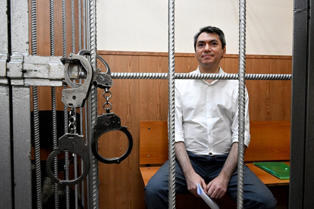 غريغوري جالس في زنزانة السجن، مع أصفاد معدنيّة معلقة على القضبان