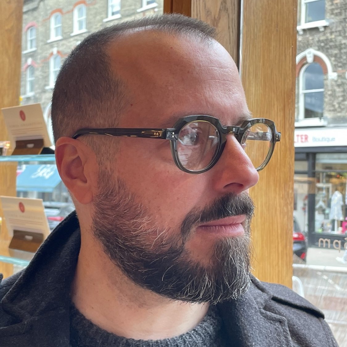 Christhian is looking to the side and wearing chunky green glasses. 