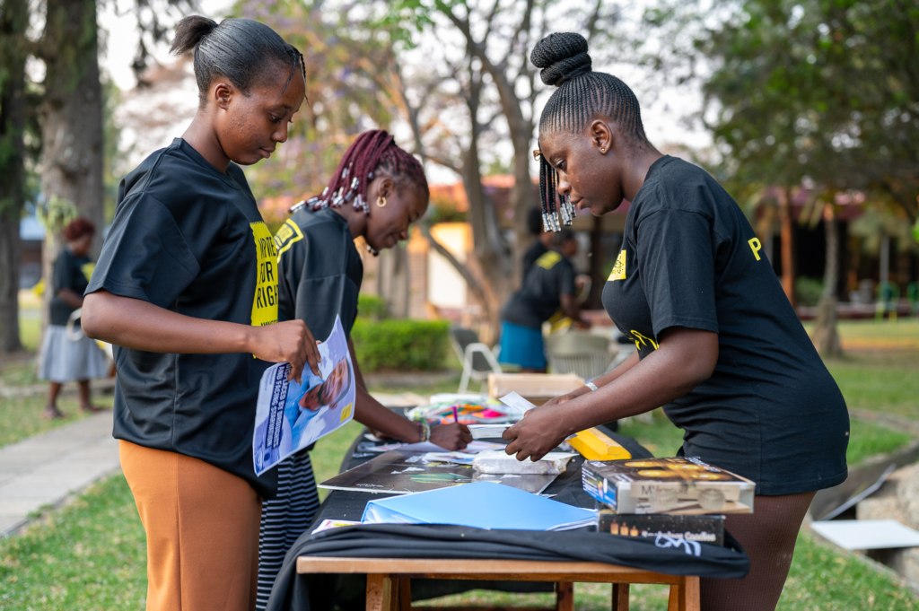 Three women, wearing black t shirts emblazoned with Write for Rights, stand at table, sorting campaign materials.
