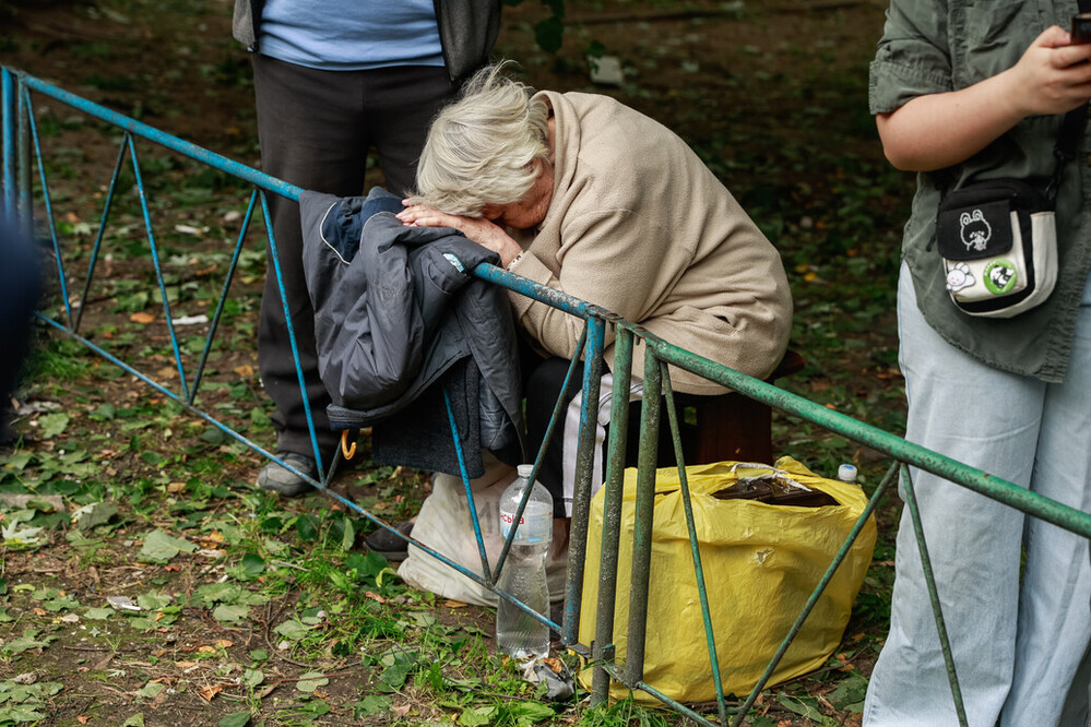 an older woman holds her head in her hands, in a state of heavy emotions as she mourns