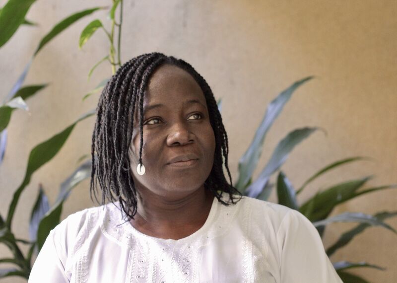 Cécile Yougbare, a Black woman with braided hair wearing a white top blazer, looks to the side as she smiles. She is an activist in Côte d'Ivoire