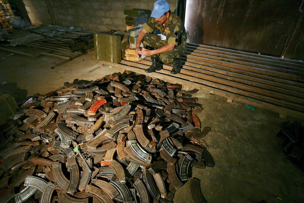 A Un peacekeeper kneels next to a large pile of AK-47 magazines, examining them. 