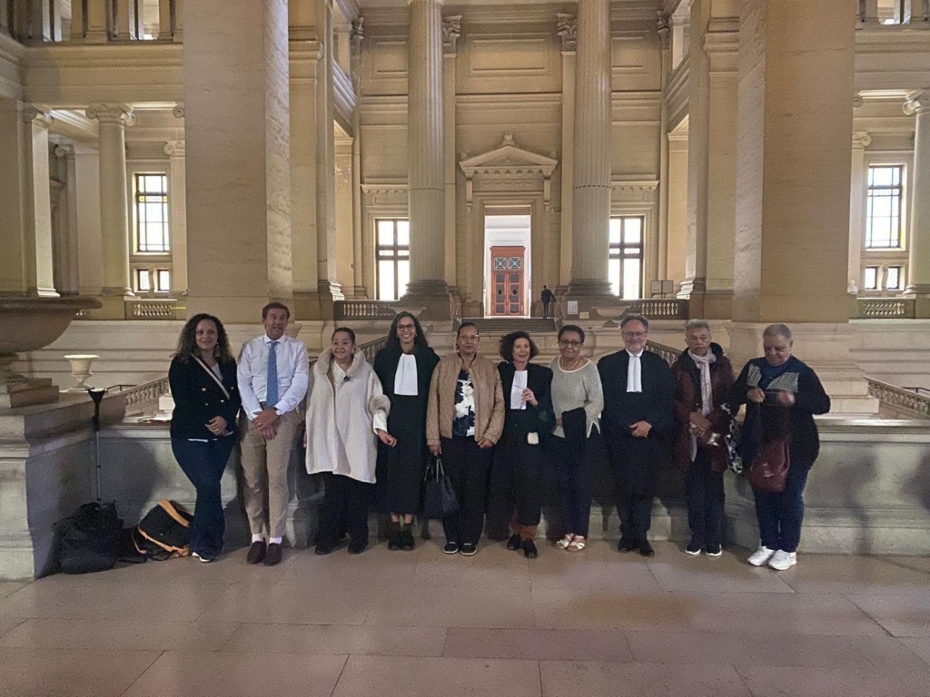 Grupo de personas de pie mirando a la cámara en un bello palacio de justicia de techos altos y suelos de mármol.