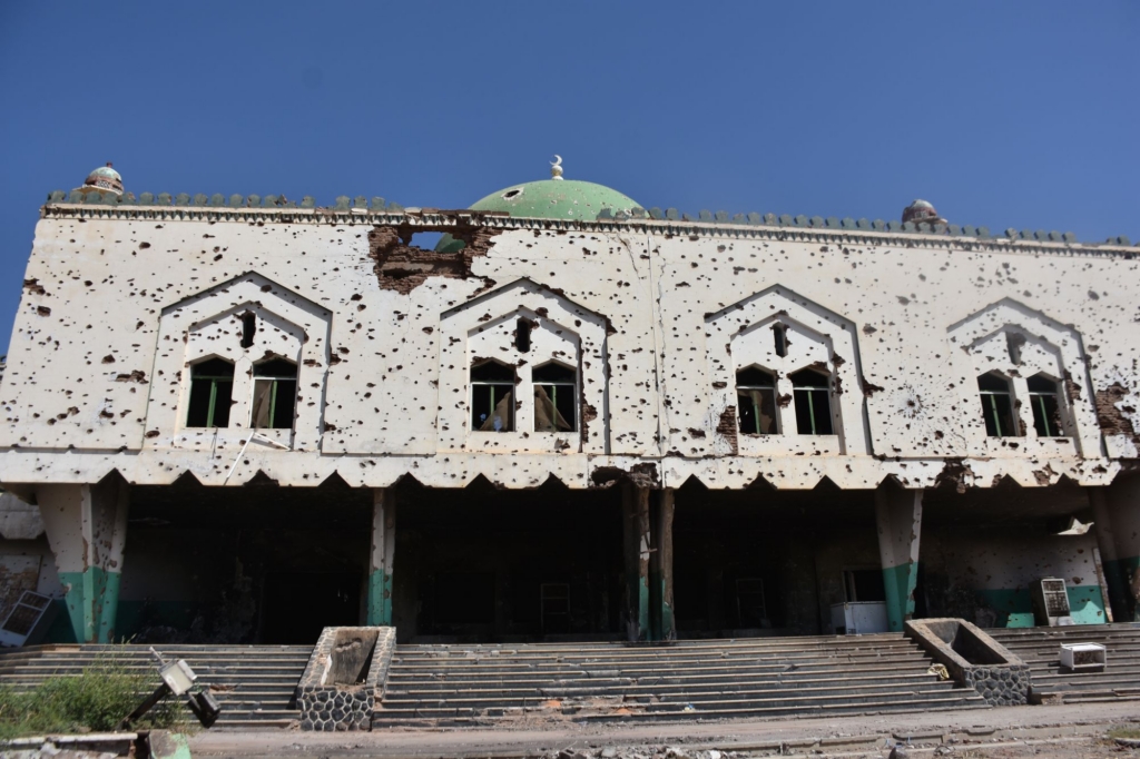 the front of a mosque. The building is covered in bullet holes. 