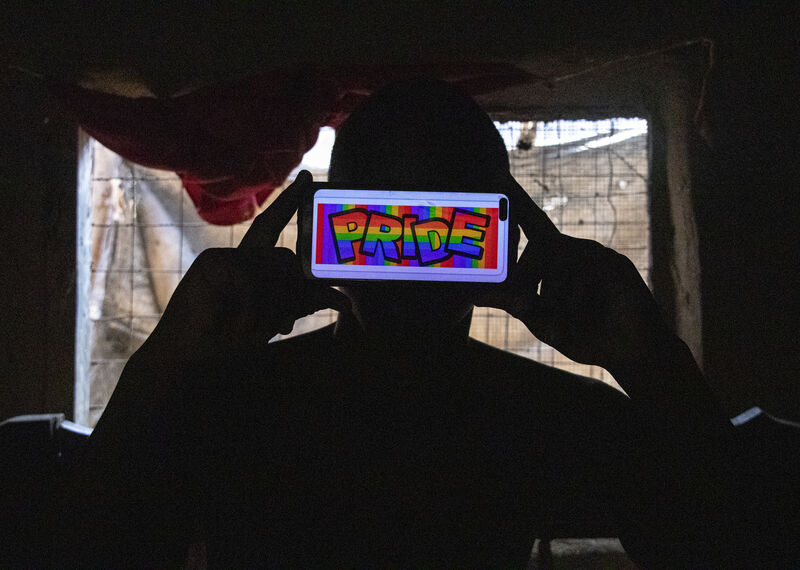 In a dark room a person holds up a mobile phone with the word "pride" displayed in bright rainbow lettering