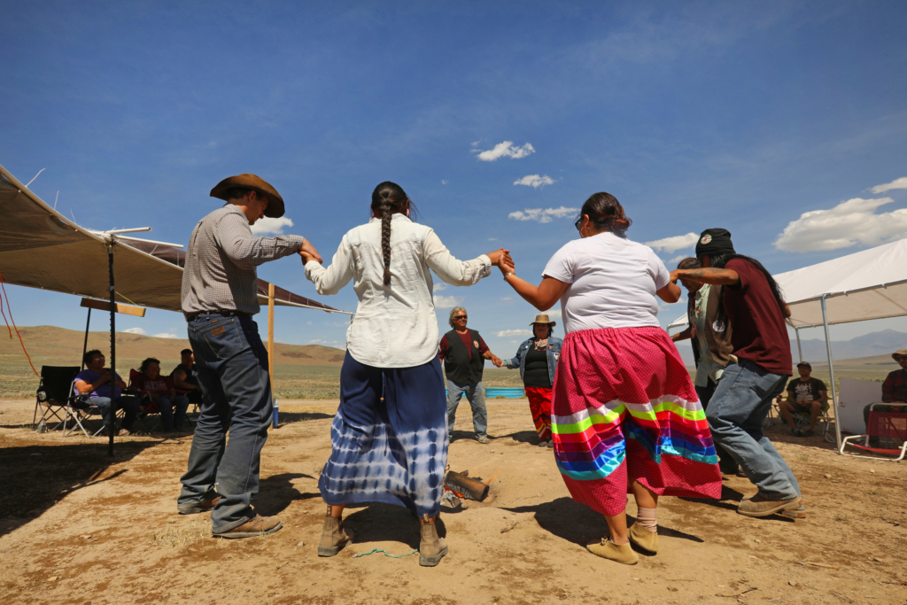 Members of the Paiute Shoshone tribe hold hands as they dance in a circle against a blue sky