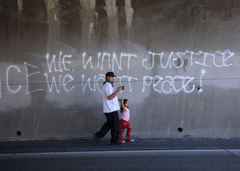 A man and little girl walk past a wall graffitti'd with the slogan "we want justice, we want peace"