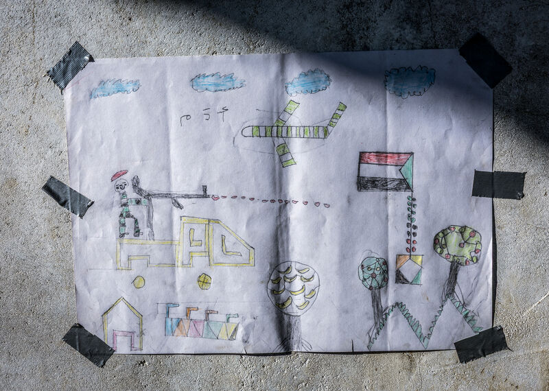 A child's drawing depicting a refugee camp with a plane flying overhead and a Sudanese flag flying
