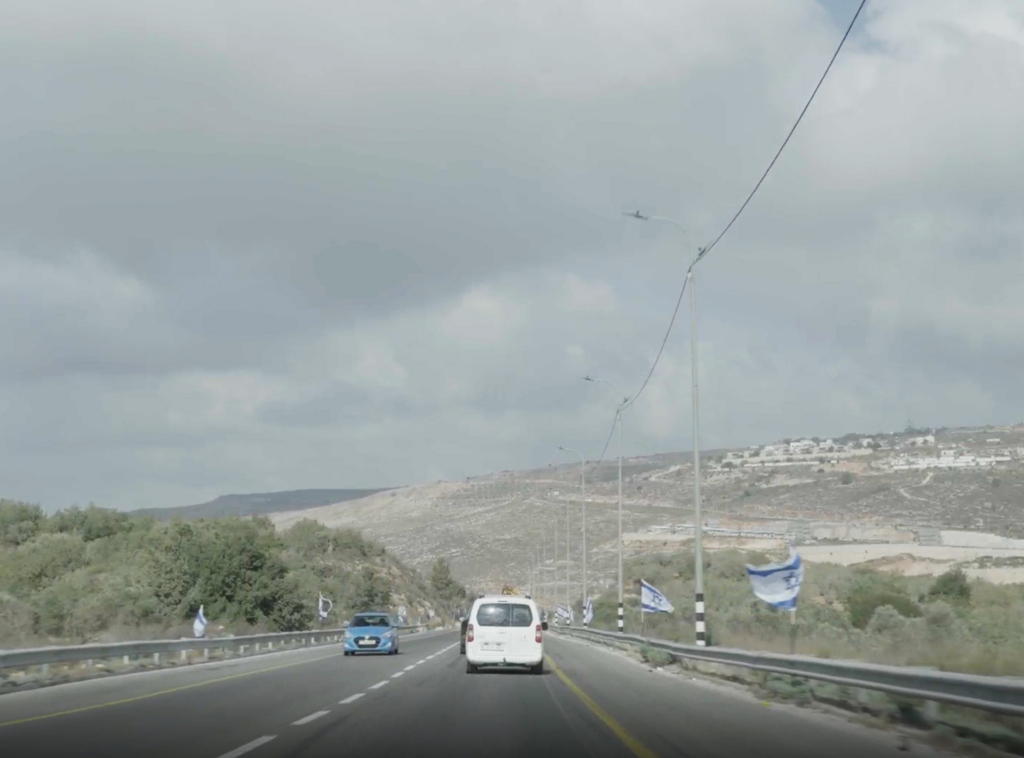 Cars pass by Israeli flags along a road